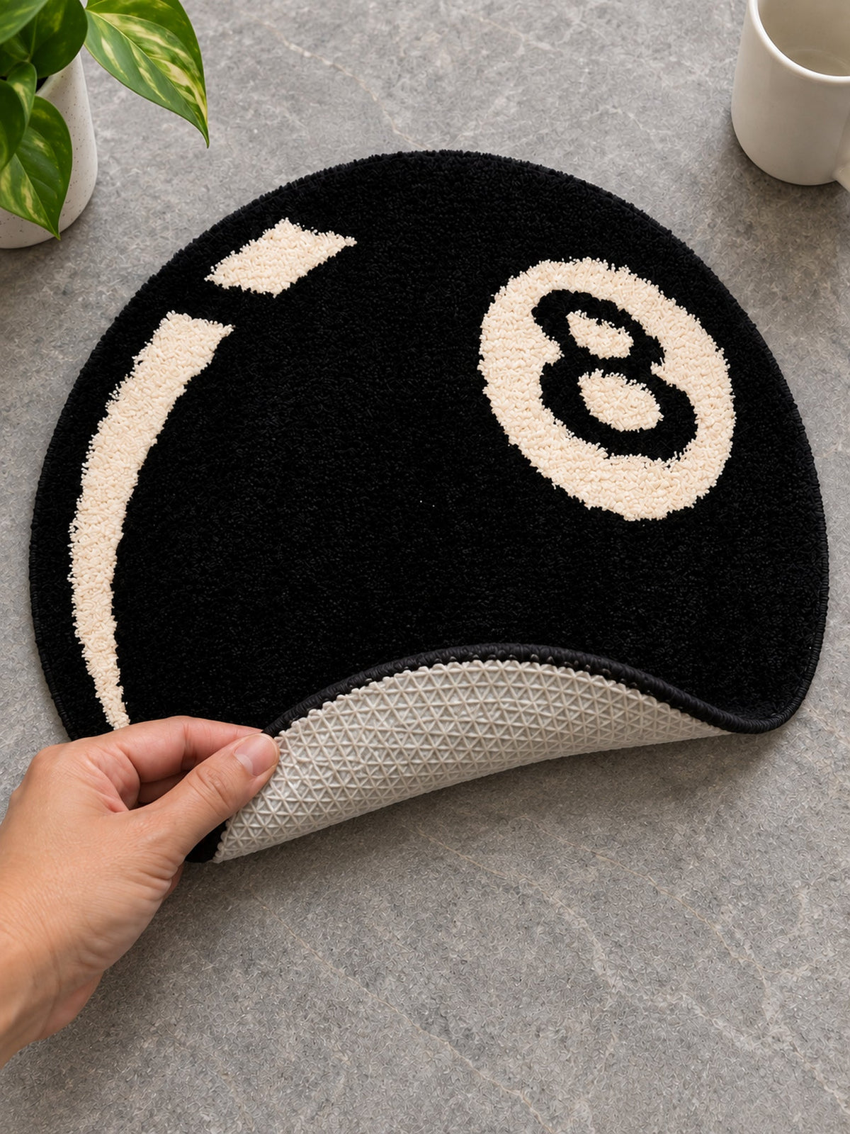 Black eight-ball round rug, 40 cm diameter, with one edge lifted to show the pale patterned backing.