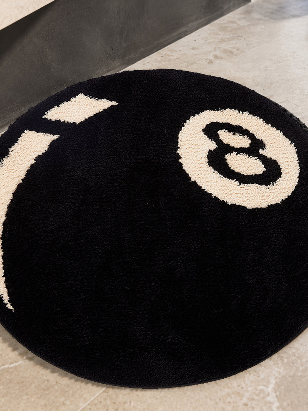 Black eight-ball round rug, 80 cm diameter, close view of the round outline and 8 motif on a bathroom floor.