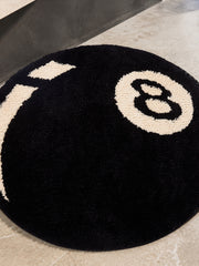 Black eight-ball round rug, 80 cm diameter, close view of the round outline and 8 motif on a bathroom floor.