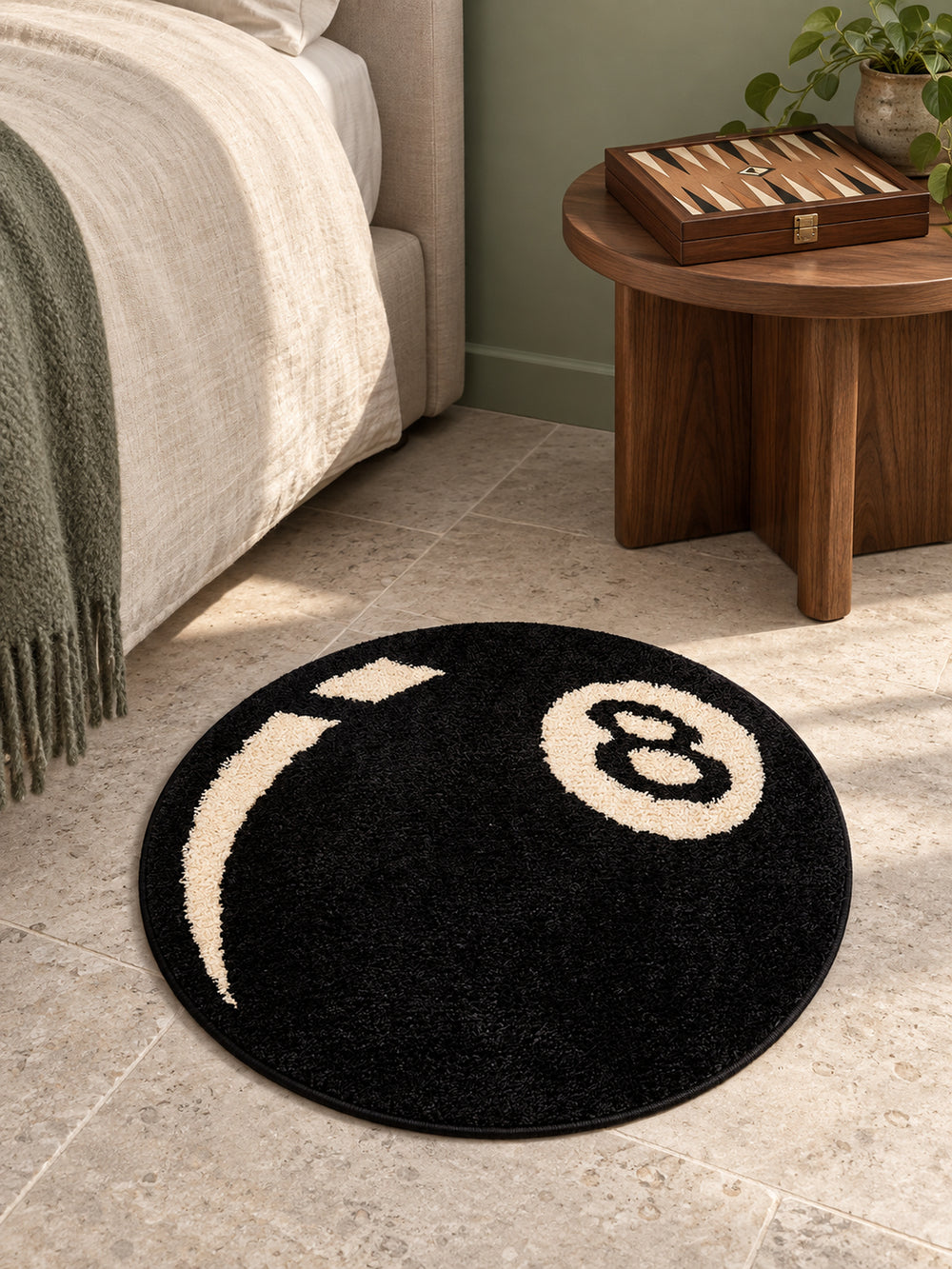Black eight-ball round rug, 40 cm diameter, beside a bed and wooden side table.