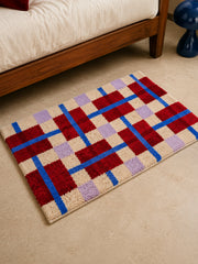 Crimson Grid Colorblock Bath Mat beside a bed, shown from another angle