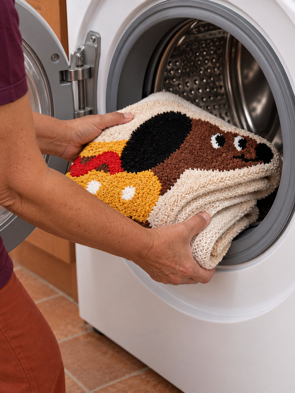 Hot dog dachshund-shaped rug, 80 x 160 cm, folded and held at the door of a front-loading washing machine.