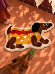 Hot dog dachshund-shaped rug, 80 x 160 cm, viewed from above beside a dachshund on terracotta tiles.
