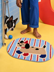 Blue and red striped playful pup mat, 50 x 80 cm, viewed from above beside a dog and bare feet at a shower.