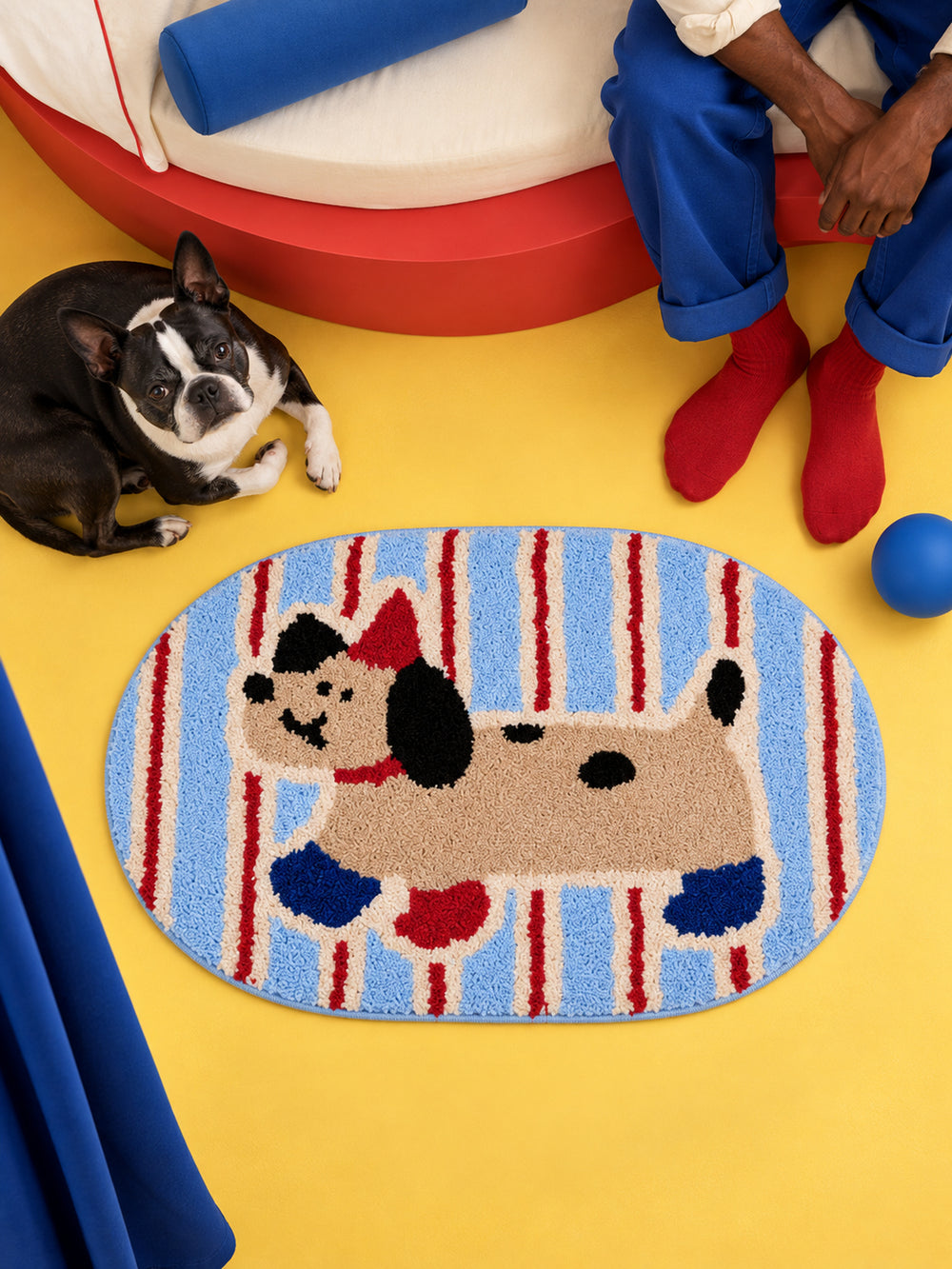 Blue and red striped playful pup mat, 50 x 80 cm, viewed from above beside a dog and curved red seat.