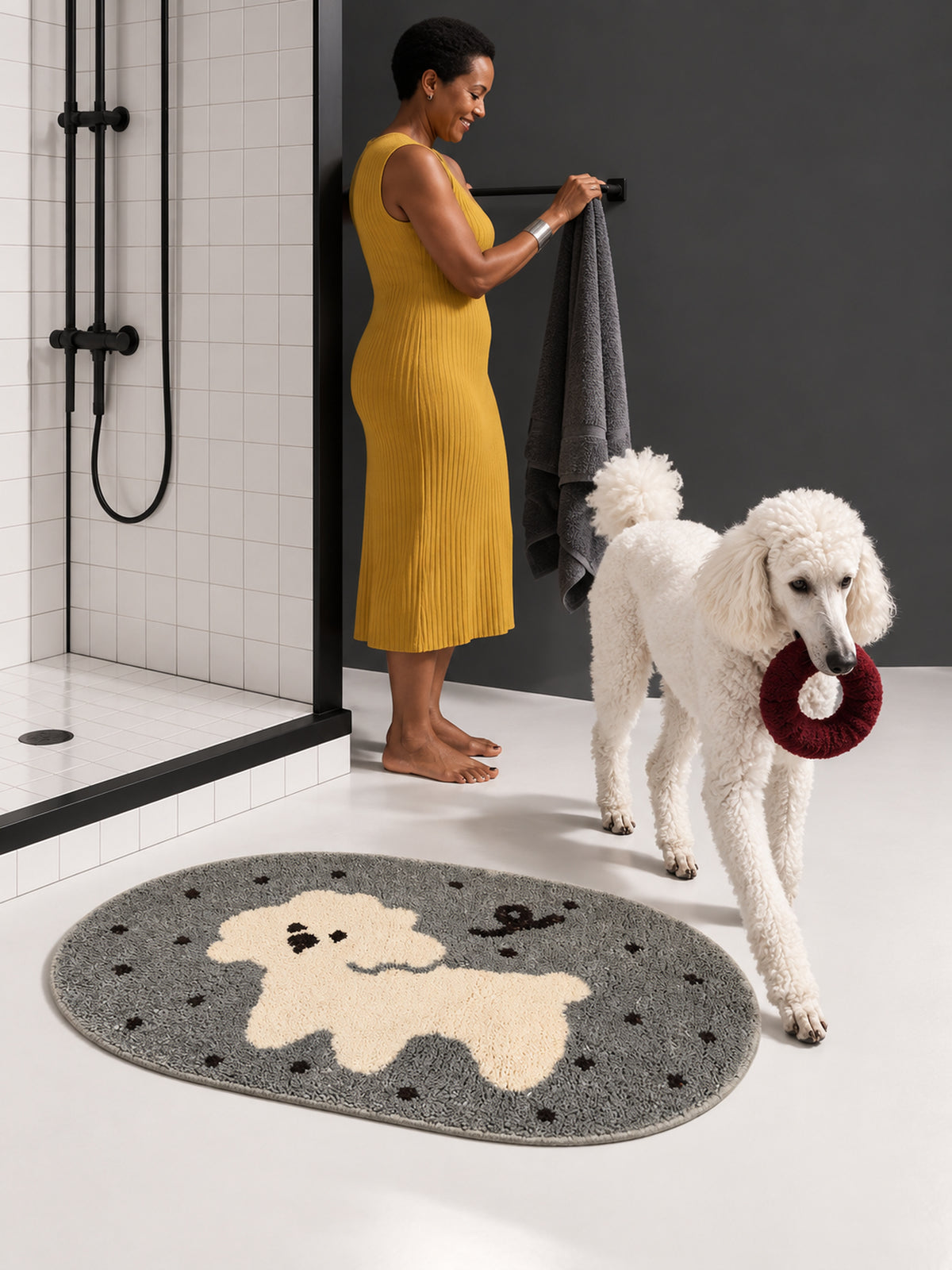 Gray polka-dot pup oval mat, 50 x 80 cm, beside a person and white poodle at a shower.