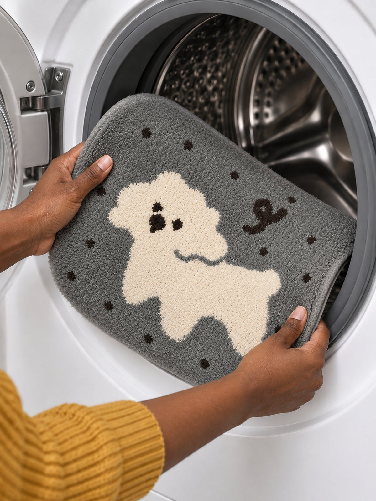 Gray polka-dot pup oval mat, 50 x 80 cm, held at the open door of a front-loading washing machine.