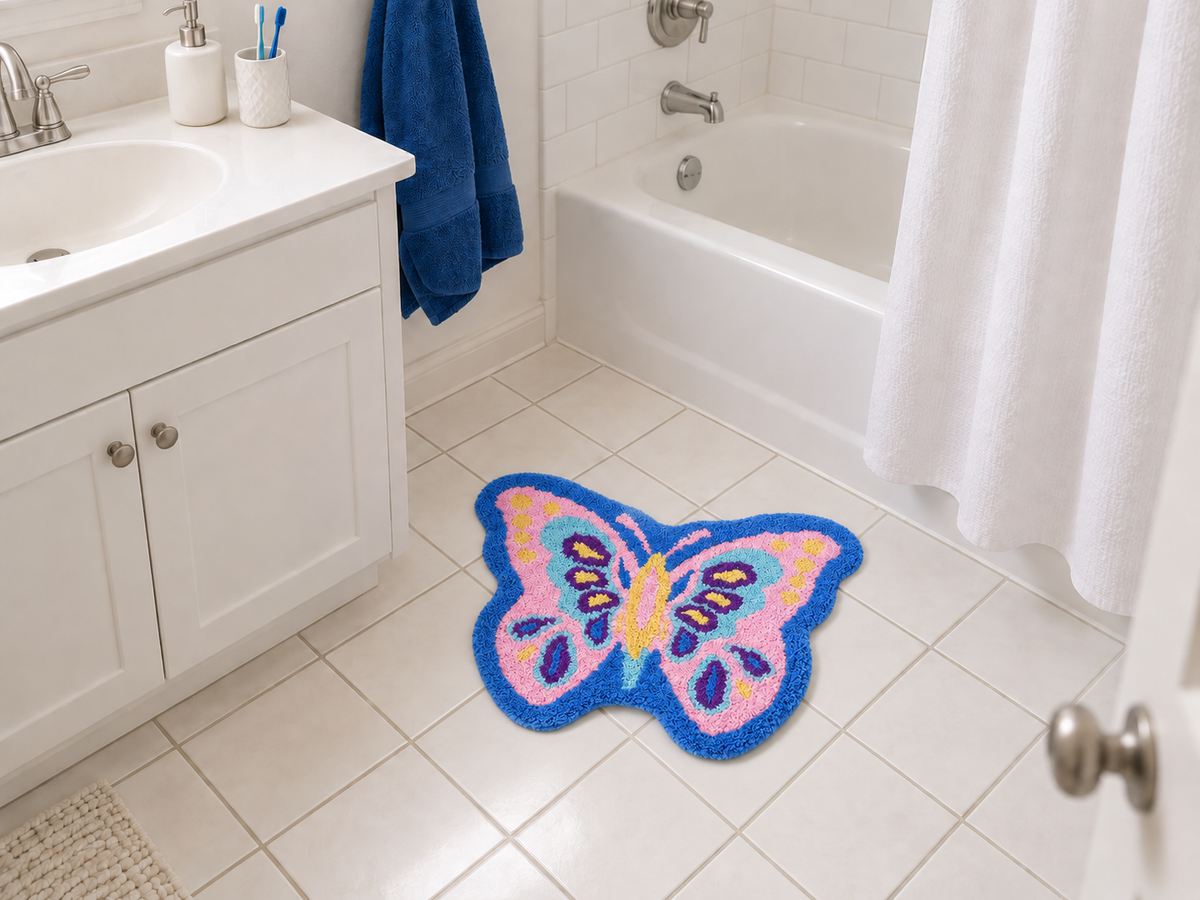 A blue and pink LivingFun butterfly bath mat beside a white vanity and tub in a compact, everyday American-style bathroom.