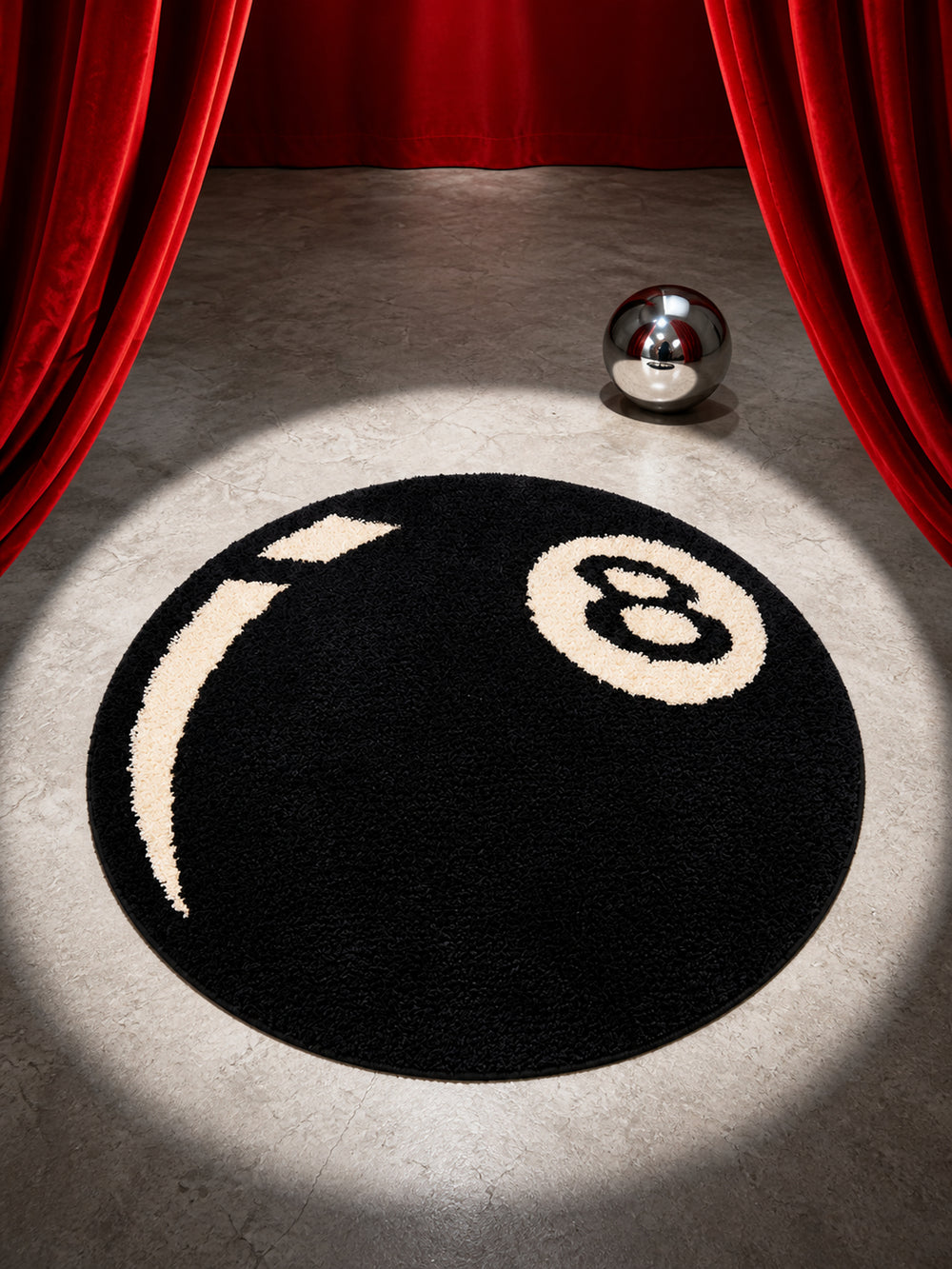 Black eight-ball round rug, 80 cm diameter, in a spotlight between red curtains.
