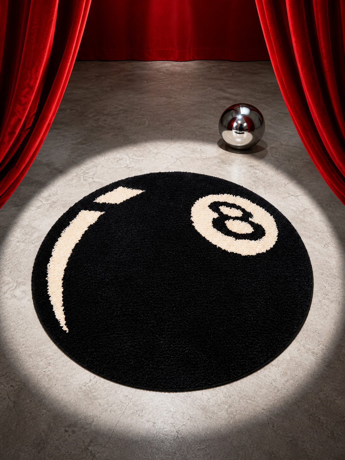 Black eight-ball round rug, 80 cm diameter, in a spotlight between red curtains.