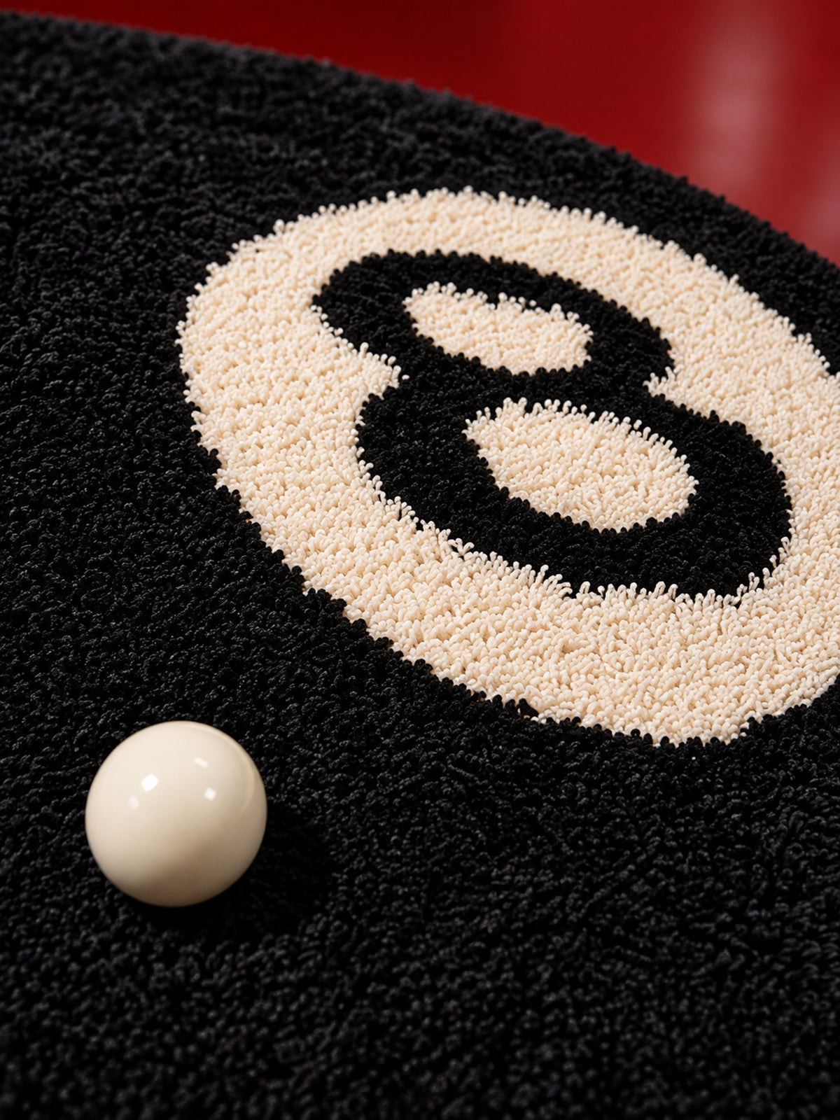 Black eight-ball round rug, 80 cm diameter, close-up of the ivory 8 motif and black pile beside a billiard ball.