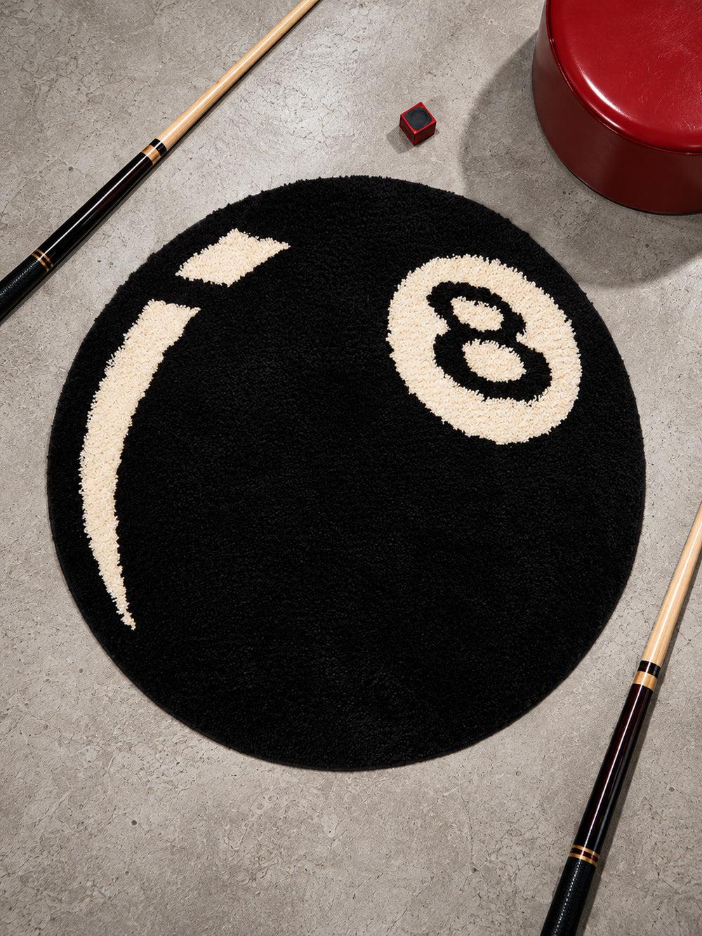 Black eight-ball round rug, 80 cm diameter, viewed from above between pool cues.