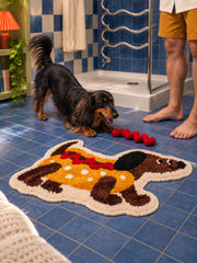 Hot dog dachshund-shaped mat, 50 x 80 cm, beside a dachshund and person at a blue-tiled shower.