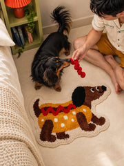 Hot dog dachshund-shaped mat, 50 x 80 cm, beside a person playing with a dachshund near a bed.