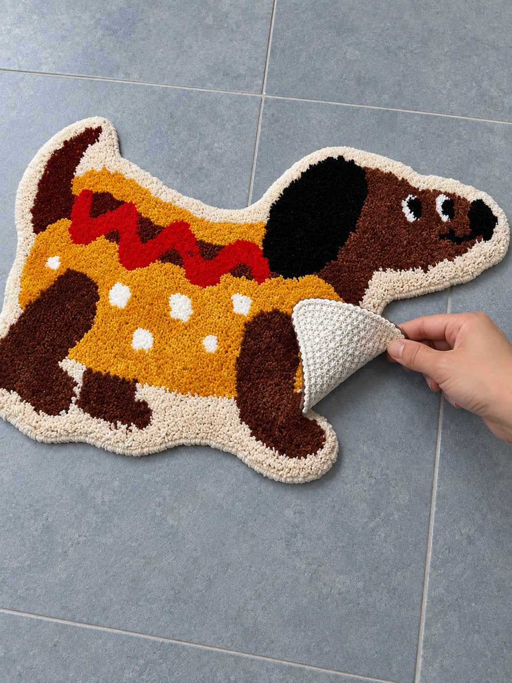 Hot dog dachshund-shaped mat, 50 x 80 cm, with an edge lifted to show the pale patterned backing.