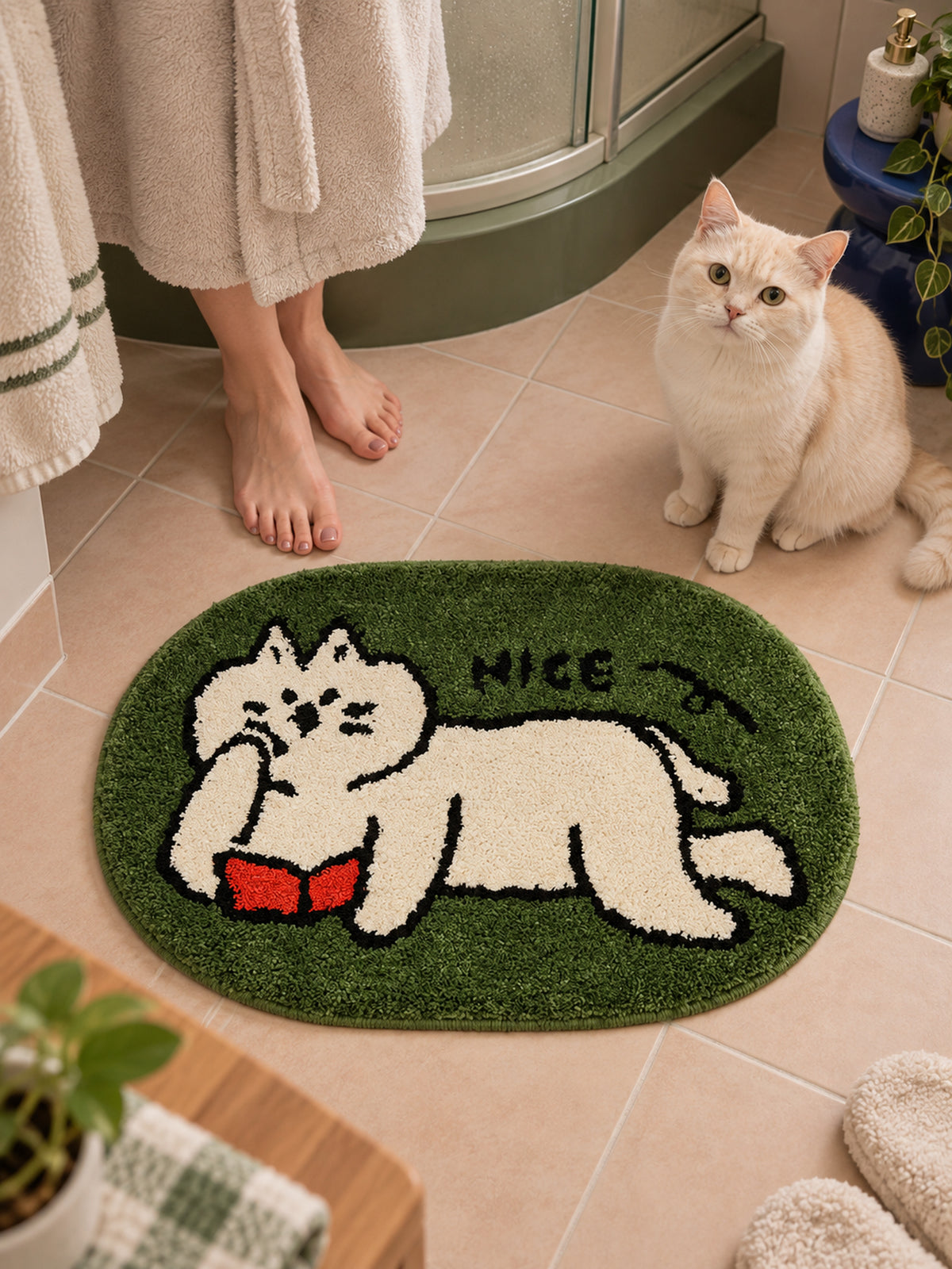 Green reading-cat oval mat, 50 x 80 cm, beside a person and cream-colored cat in a bathroom.