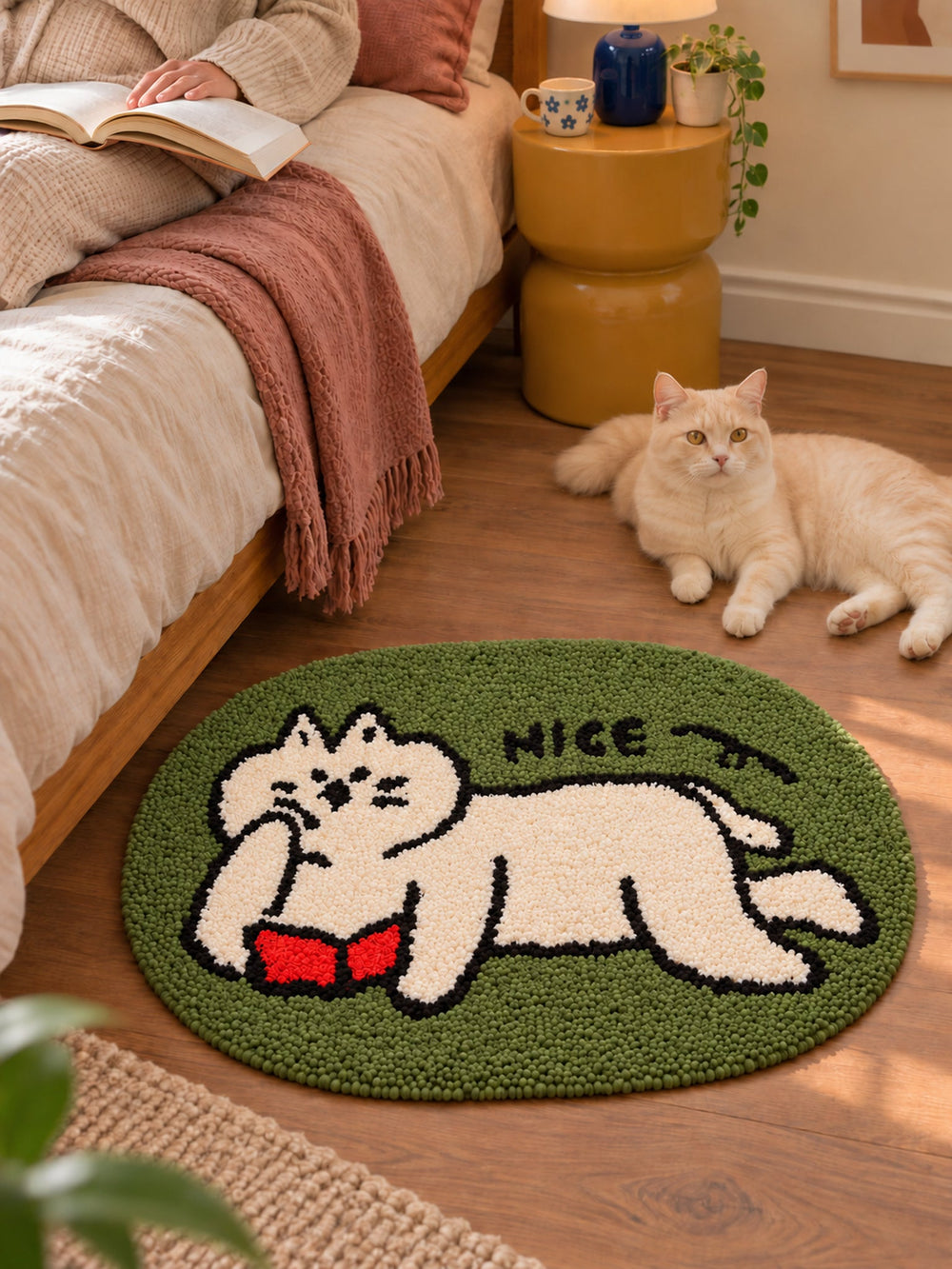 Green reading-cat oval mat, 50 x 80 cm, beside a bed, a reader and a cream-colored cat.