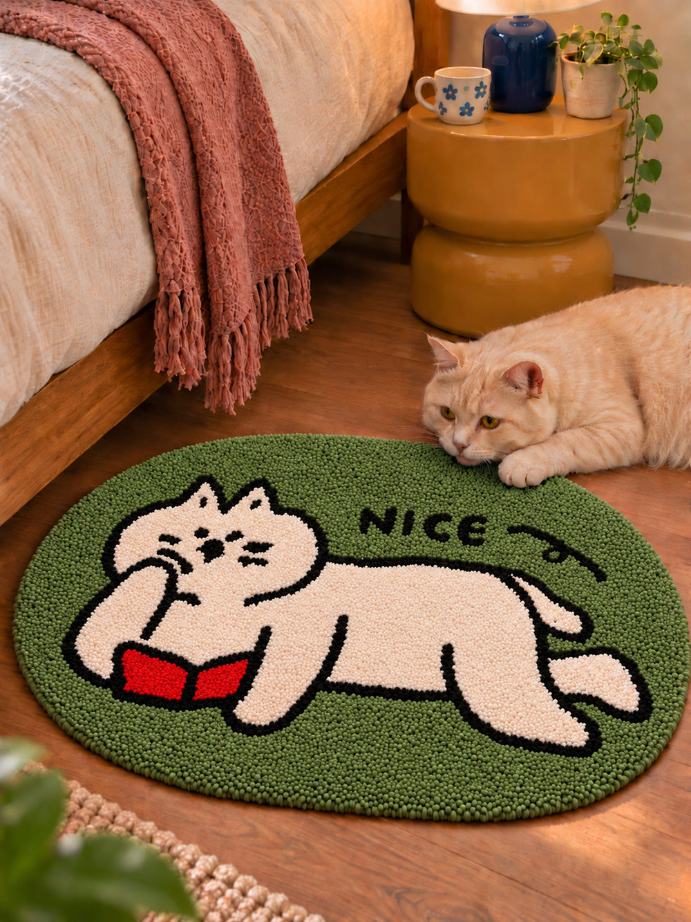 Green reading-cat oval mat, 50 x 80 cm, beside a bed with a cat resting at its edge.