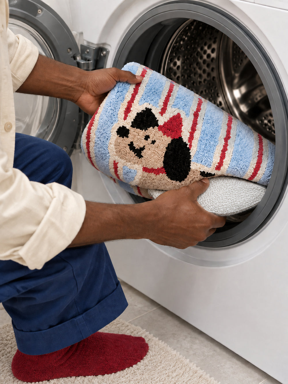 Blue and red striped playful pup mat, 50 x 80 cm, being placed into a front-loading washing machine.