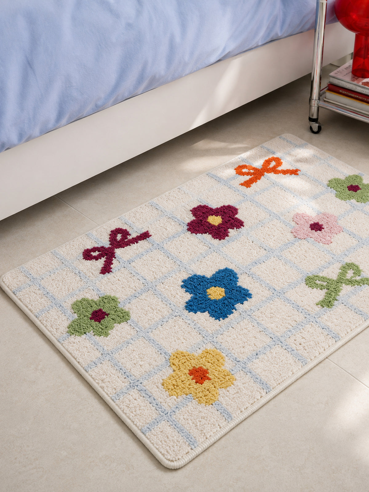 Garden Bows and Blooms checkered mat, 50 x 80 cm, close view beside a blue-covered bed.